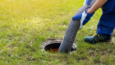 Man with gloves holding septic pump in hole in grassy yard